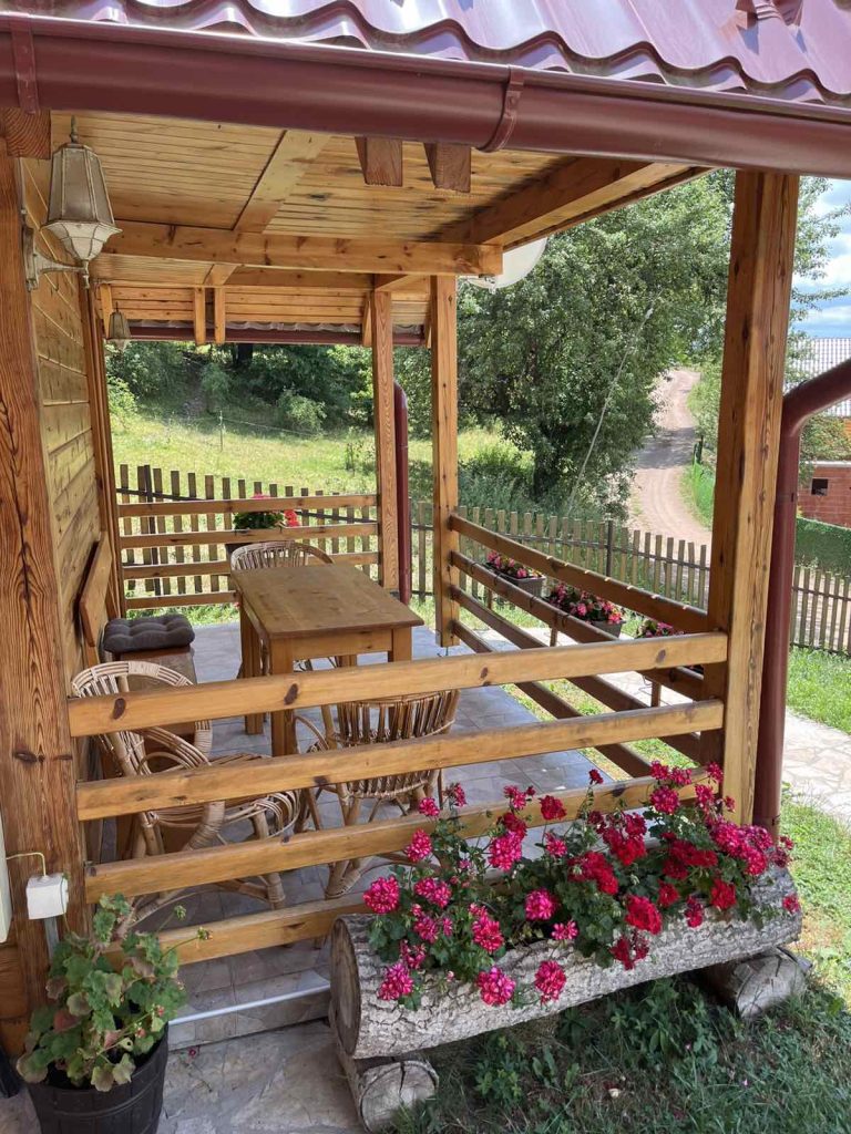 Drveni sto i pletene stolice ispred brvnare Drveni Raj Uvac okruženi prirodom