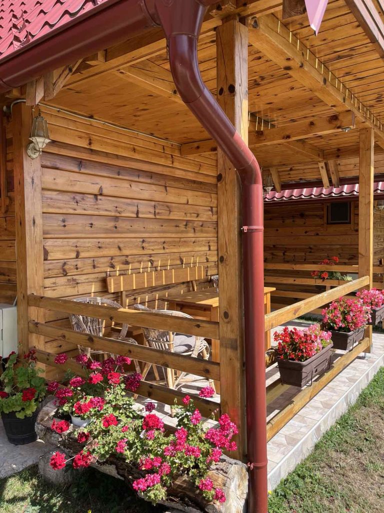 Uredjen prostor ispred kuće sa drvenim stolom, stolicama i cvećem